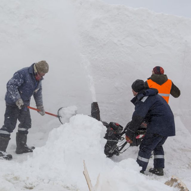 Workers remove snow in a blizzard using a snowplow